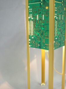 Vue côtés lampe verte et dorée allumée et réalisée avec des circuits imprimés. Piètement laitonné 4 pieds avec ses reflets