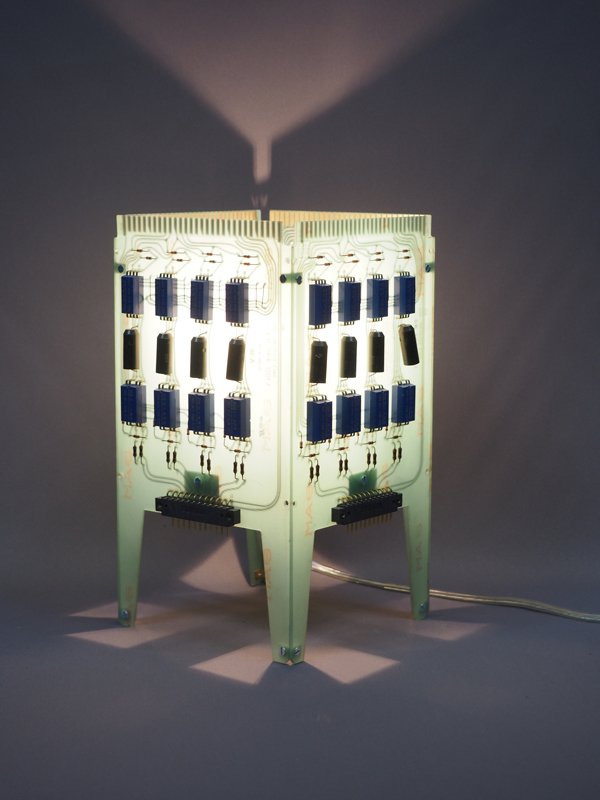 Lampe fond vert avec des composants bleus allumée et réalisée avec des cartes électroniques. Piètement 4 pieds avec ses reflets