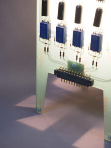 Vue côté lampe fond vert avec des composants bleus allumée et réalisée avec des cartes électroniques. Piètement 4 pieds avec ses reflets