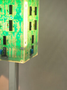 Vue côtés lampe verte et argentée allumée réalisée avec des cartes électroniques et un piètement en acier chromé avec ses reflets