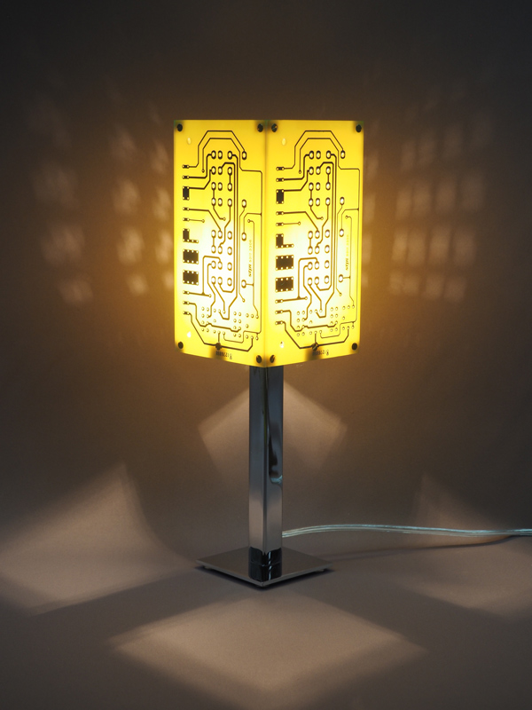 Lampe jaune et argentée allumée réalisée avec des cartes électroniques et un piètement en acier chromé avec ses reflets