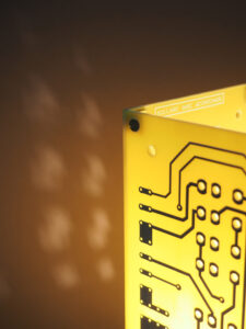 Vue haut lampe jaune et argentée allumée réalisée avec des cartes électroniques et un piètement en acier chromé avec ses reflets