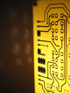 Vue côté lampe jaune et argentée allumée réalisée avec des cartes électroniques et un piètement en acier chromé avec ses reflets